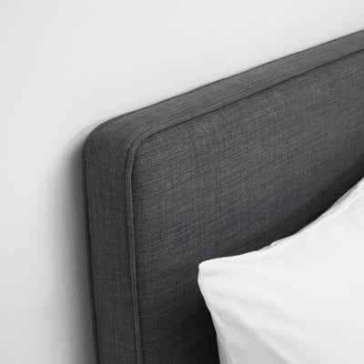 Close-up of grey upholstered headboard, well-crafted with neat stitching, leaning against plain wall.