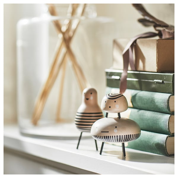 Two wooden figures on shelf, one striped body, other round. Books and vase in background.