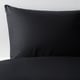Close-up of sleek, black DVALA pillowcase made of soft, natural cotton, resting on dark bedding.