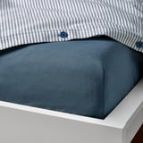 Bed fitted sheet with blue stripe pillow cover, dark blue fabric, white bed frame.
