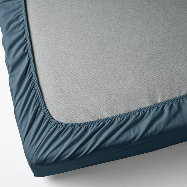 Corner of gray mattress with blue fitted sheet.