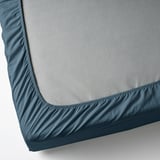 Corner of gray mattress with blue fitted sheet.