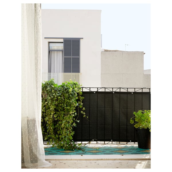 Modern balcony with white curtain, black privacy screen, green plants, and neighboring white building.