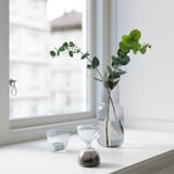 Clear hourglass next to green plants and tealight near the window.