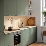 Modern kitchen with green EKBACKEN cabinets, stainless steel oven & sink, wooden countertop, and light floor.
