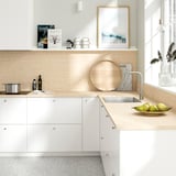 Modern kitchen featuring EKBACKEN light wooden countertop, white cabinets, stainless sink, and silver faucet. Decorated with bowls and cookbooks.