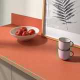 A kitchen countertop with a bowl of pomegranates and stacked mugs, ideal for easy cleaning and maintenance, with a 25-year guarantee.