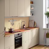 Modern kitchen with creamy EKBACKEN worktop & oven. Wooden backsplash, potted plant next to window.