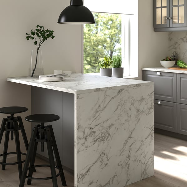 Kitchen island with marble-patterned top, black stools, pendant lamp, grey cabinets.