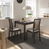 Modern kitchen nook with small brown EKEDALEN table and chairs, white cabinets, large windows, and a hanging white lamp.