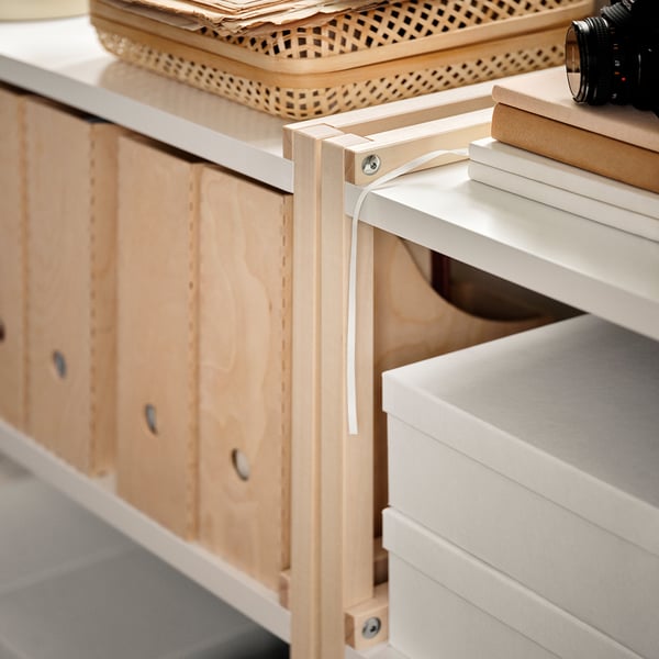 An EKENABBEN light wooden shelving unit with white shelves holding boxes and a camera on top.