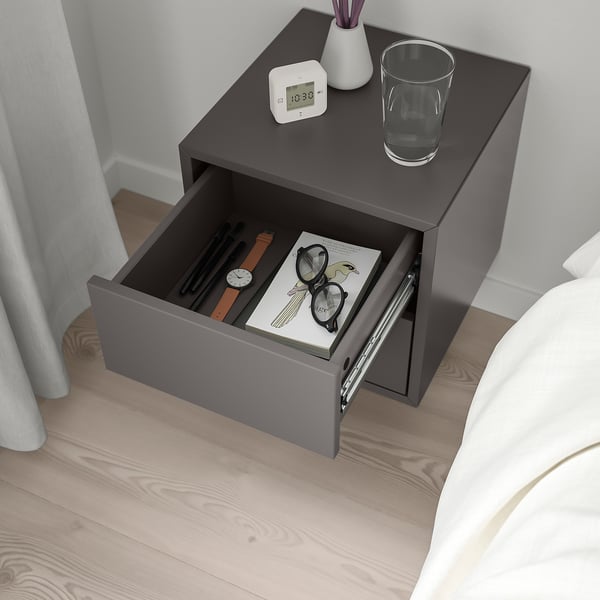 Bedside table with open drawer, clock, glass, and vase on top.