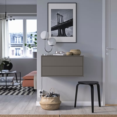 Modern room: black framed bridge art, wall-mounted lamp, grey cabinet with drawers, orange bench, black stool, large basket with keys.