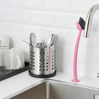 Kitchen scene with stainless cutlery organizer on counter and pink brush beside sink.