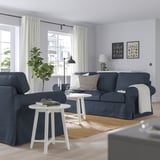 Blue sofa, throw, cushions in living room. Large window, art, cozy vibe.