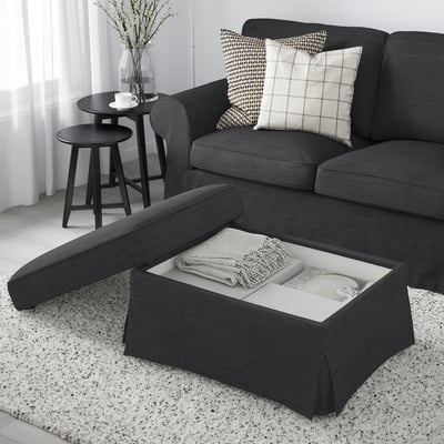Modern living room with gray EKTORP footstool featuring storage. Sofa with black and white pillows, side table with cup and flowers.