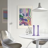 Modern dining area with white table, clear chairs, purple candlesticks, flowers, abstract art, and large pendant lamp.