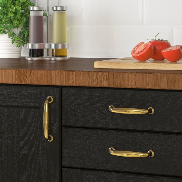Black kitchen cabinets with brass handles displaying a cutting board and fresh tomatoes on a wooden countertop.