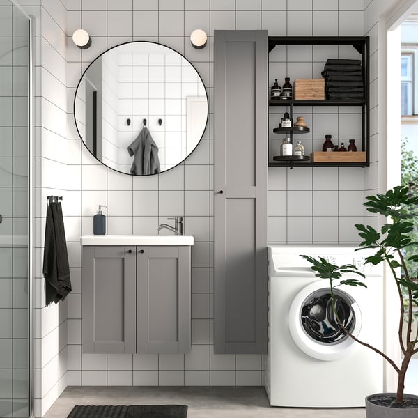 Modern bathroom with gray ENHET cabinets, round mirror, white washing machine, and green plant.