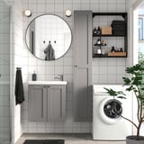 Modern bathroom with gray ENHET cabinets, round mirror, white washing machine, and green plant.