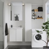 Modern bathroom with white ENHET cabinet, mirror, sink, and washing machine. Shelves hold towels and toiletries.