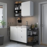 Small, modern white kitchen set with clean lines. Cabinets, open shelves, and accessories; stainless steel sink and appliances; greenery adds warmth.