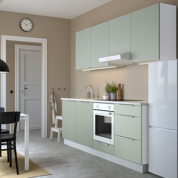 Modern kitchen with pale green cabinets, white appliances, black chairs, and white clock. The cabinets are sleek and offer ample storage.
