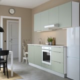 Modern kitchen with pale green cabinets, white appliances, black chairs, and white clock. The cabinets are sleek and offer ample storage.