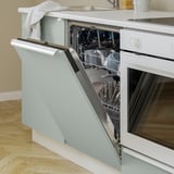 Open dishwasher in kitchen with clean dishes, light blue cabinet.