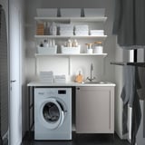 White ENHET laundry station with shelves, sink, washing machine, and grey towels.
