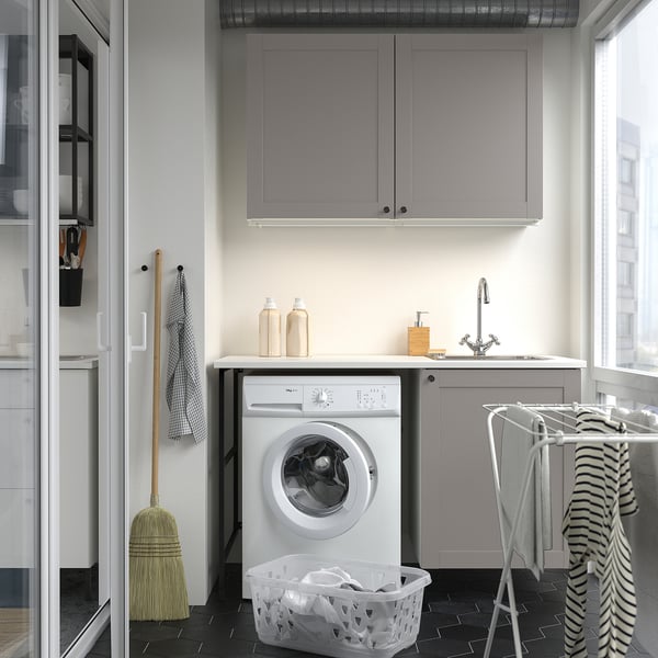 Modern laundry setup with grey cabinets, front-loading machine, small sink, and organized storage.