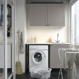 Modern laundry setup with grey cabinets, front-loading machine, small sink, and organized storage.