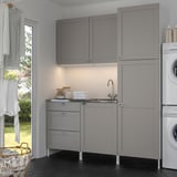 Modern grey laundry unit with sink, cabinets, and washer next to window.