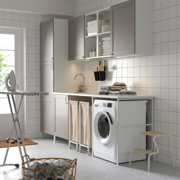 Modern laundry setup with ENHET cabinet, sink, washing machine, and drying rack. Grey and white tones, ample storage.