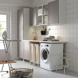 Modern laundry setup with ENHET cabinet, sink, washing machine, and drying rack. Grey and white tones, ample storage.