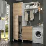 Modern laundry setup with ENHET wooden cabinet, sink, washing machine, and drying rack. Clothes hang and fold neatly.