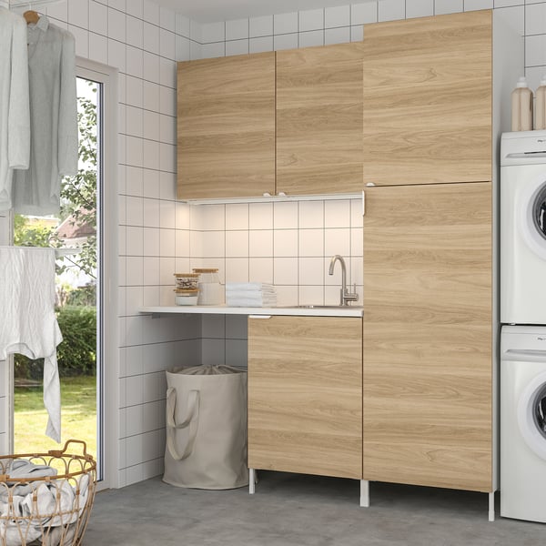 Modern laundry setup with ENHET light oak cabinets & white tiles, larger than surrounding items.