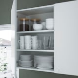 Open white kitchen cabinet showing organized dishes: plates, bowls, mugs, and glasses neatly stacked on shelves.