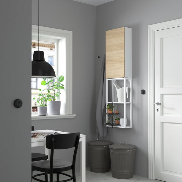 Minimalist home office with white cabinet, desk, and black chair. Modern aesthetics with potted plant and window view.
