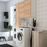 Modern laundry setup with white ENHET cabinets, washing machine, wooden doors, black accents, and tiled walls.