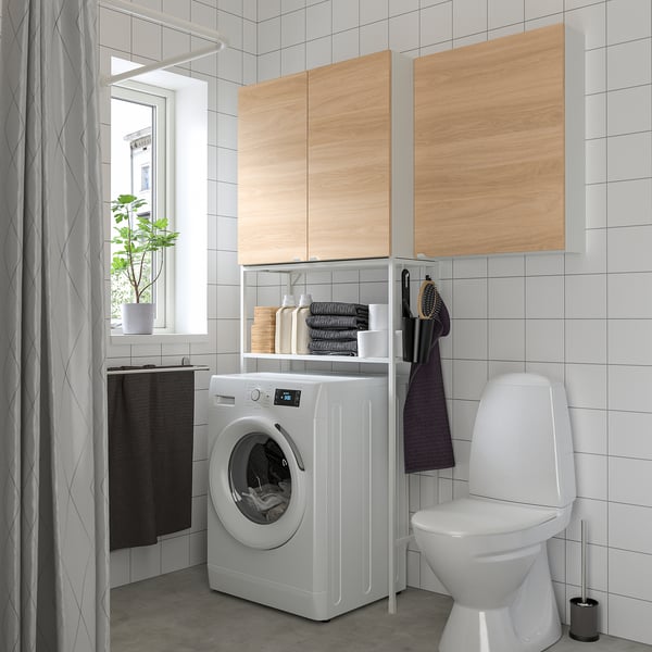 Modern bathroom ENHET storage combo, white washing machine, toilet, and wooden cabinets. Provides ample storage with open and closed shelves.