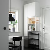 Modern room with white storage, black trolley, stool, & lamp. Natural light, plant.