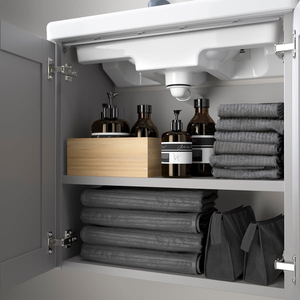 Open bathroom cabinet showing towels, bottles, and organizer.