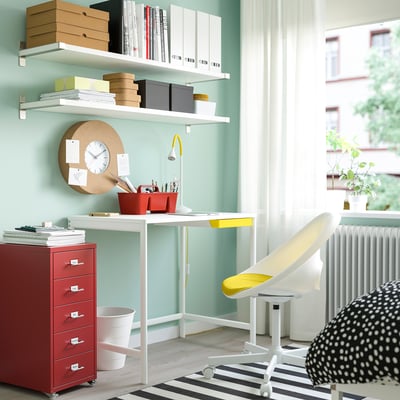 Turquoise office with desk, red drawers, yellow chair, books, and rug.