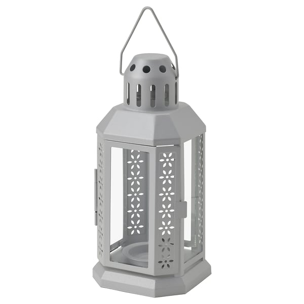Light gray ENRUM lantern, hexagonal shape, made of steel and glass, with floral cutouts and handle on top.