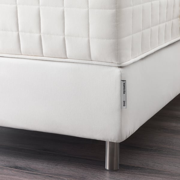 White bed base with metal legs and label on wooden floor.
