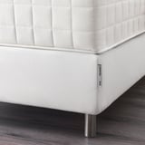 White bed base with metal legs and label on wooden floor.