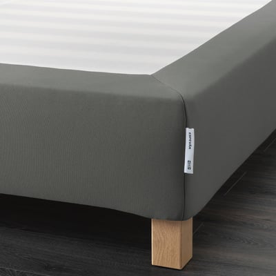 A corner of a gray bed frame on wooden legs, designed to elevate the bed and support the mattress.