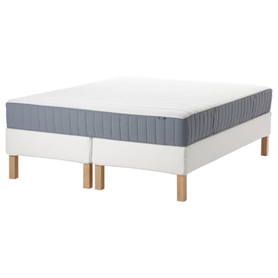 Modern white bed with gray mattress, wooden legs, upholstered base.