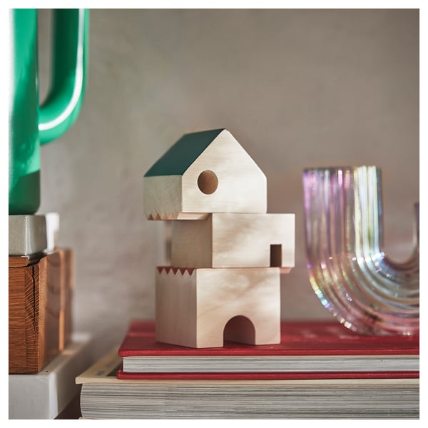 Wooden block toys in colors, stacked on books, with a clear glass vase on the side.